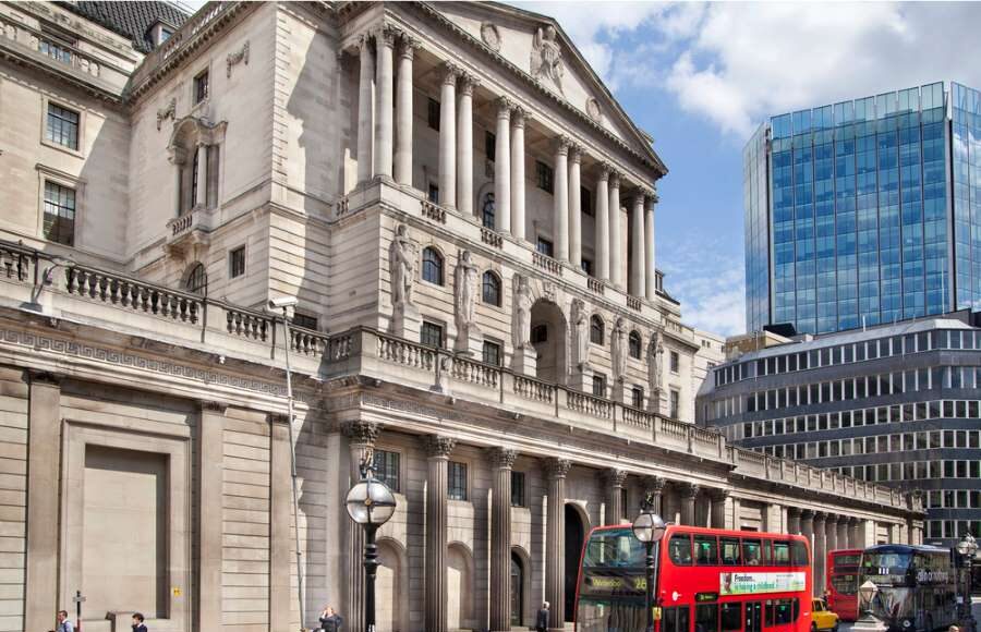 Photograph of the historic Bank of England building in London, with double-decker buses passing by — symbolizing the central bank’s role in shaping UK financial policy and the future of the digital pound.