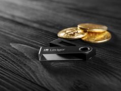 Is Ledger Preparing for an IPO? Here’s Why It Would Make Sense Ledger hardware wallet on wood background next to a stack of golden Bitcoin coins.